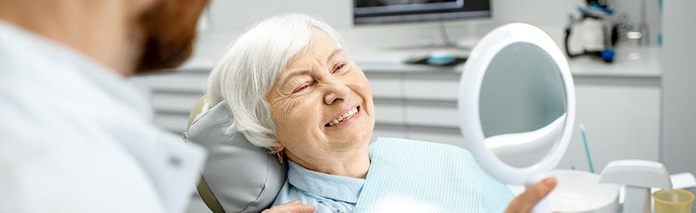 Older woman in dental chair looking at her smile