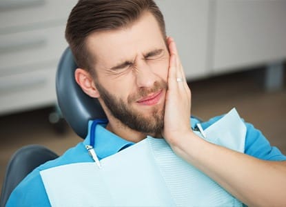 Man in dental chair holding jaw