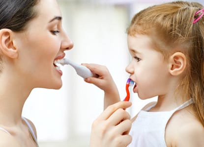 A mother and daughter brushing each other’s teeth.