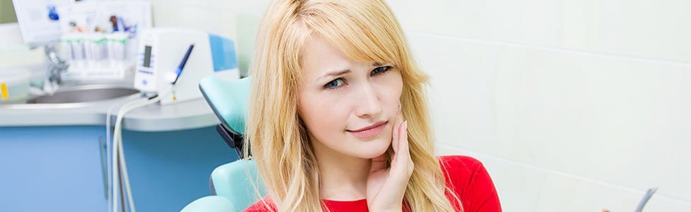 Woman in dental chair holding jaw