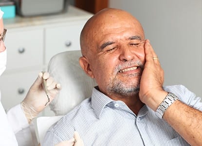Older man in dental chair holding jaw