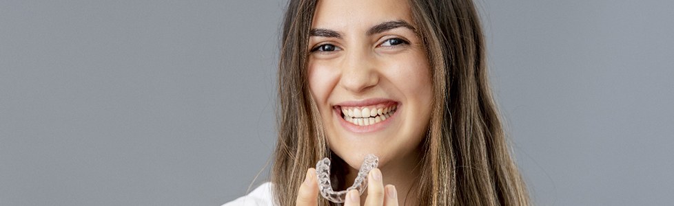 person smiling and holding their Invisalign tray