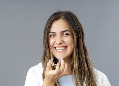 A teenage girl holding an Invisalign aligner in her hand and preparing to insert it into her mouth