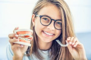 person holding a pair of Invisalign aligners and braces